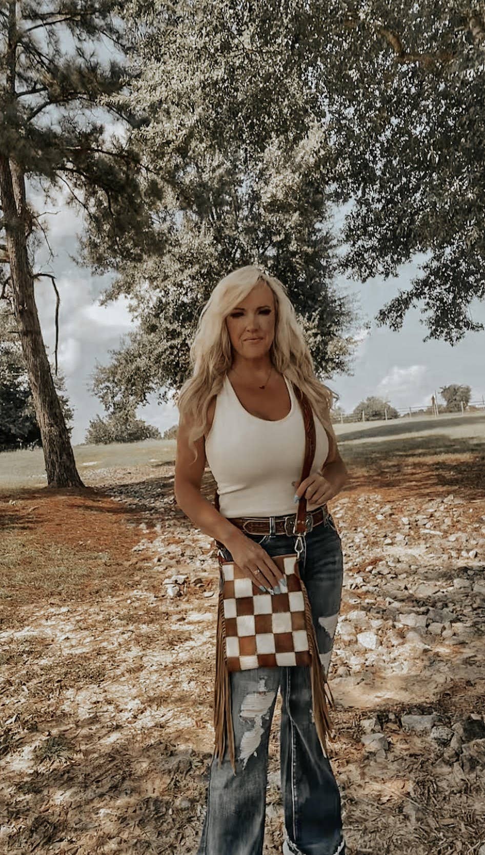 Woman standing outdoors with a checkered bag, trees and grass in the background