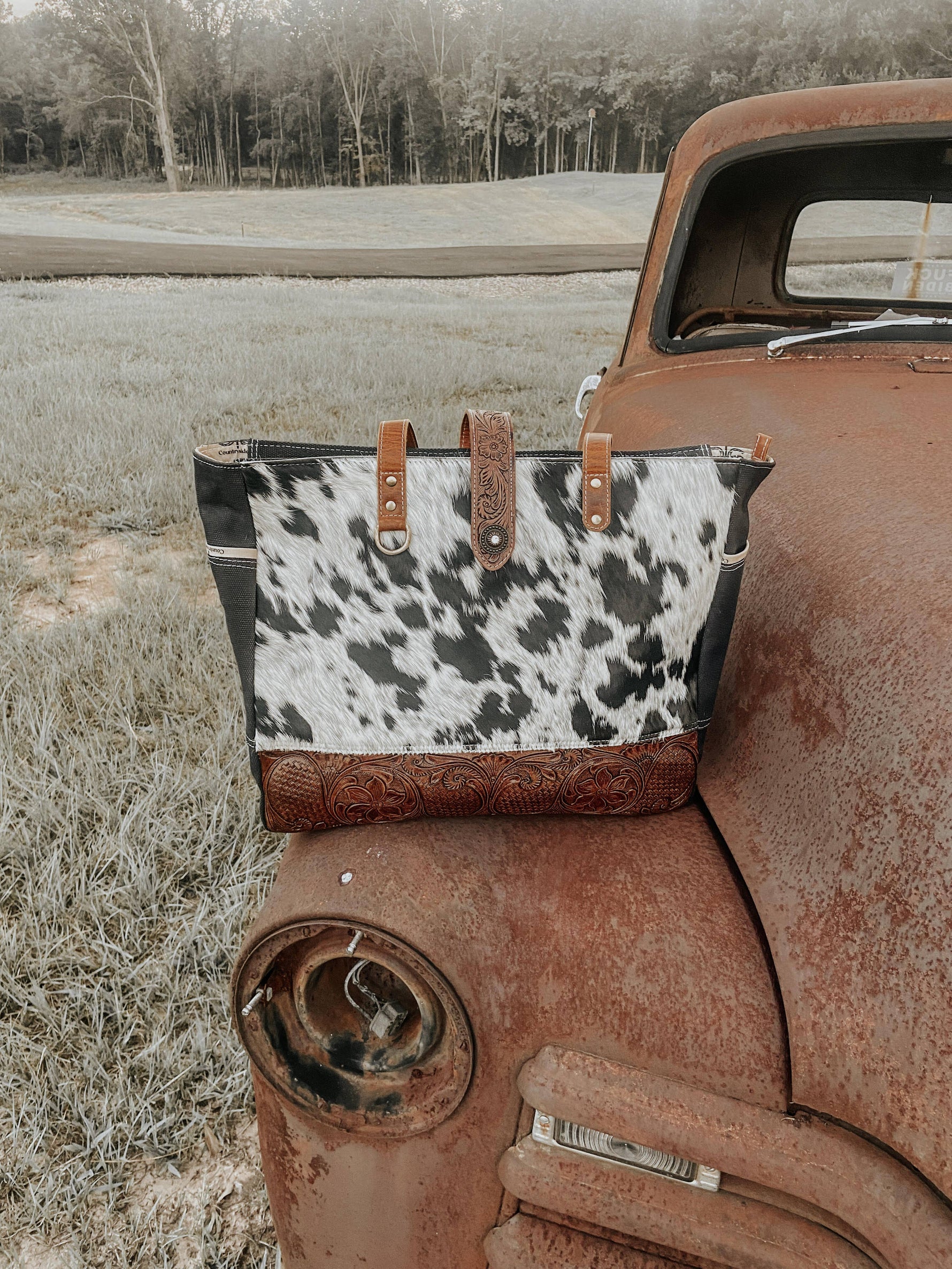 Cow print bag on an old rusted truck in a field