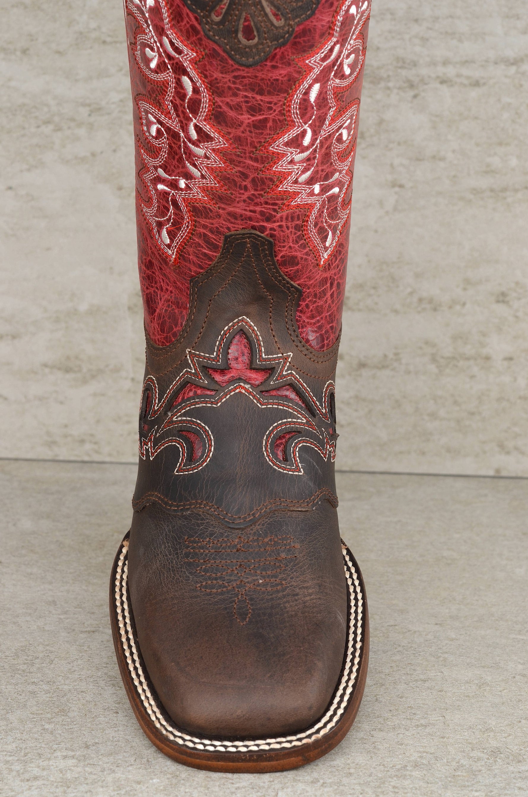 Brown cowboy boot with red interior on a wooden floor