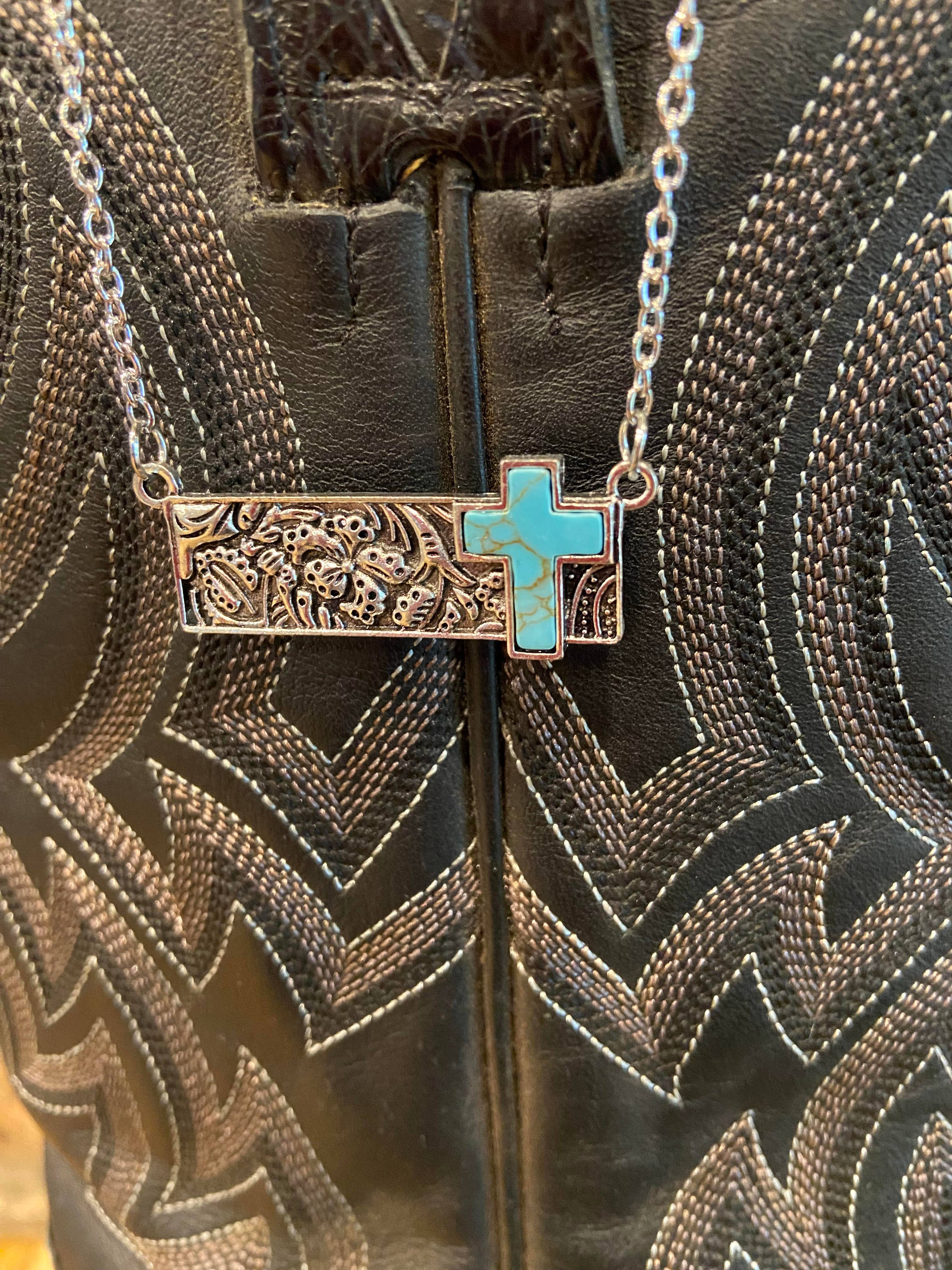 Necklace with a turquoise cross pendant on a patterned surface