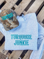 Light blue sweatshirt with 'Turquoise Junkie' text and camouflage cap on a wooden surface