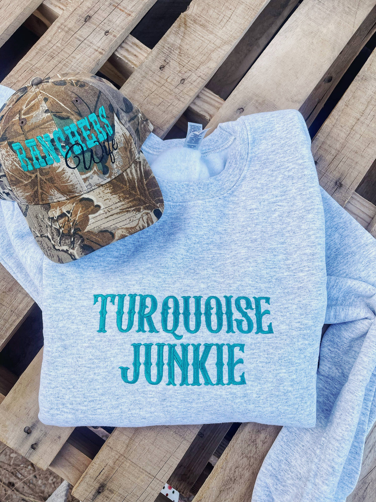 Light blue sweatshirt with 'Turquoise Junkie' text and camouflage cap on a wooden surface