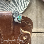 Close-up of a leather boot with a decorative brooch featuring turquoise stones, on a wooden surface with 'Countryside Co' branding.