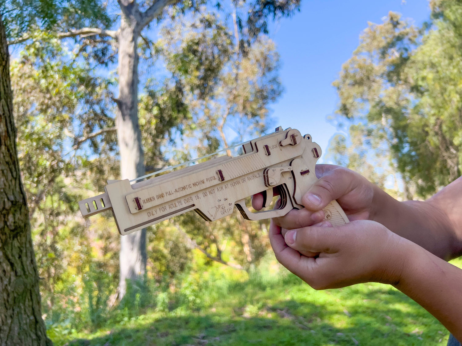Wooden gun model held by a person outdoors with trees in the background