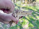 Wooden toy gun held by a hand with a blurred green outdoor background