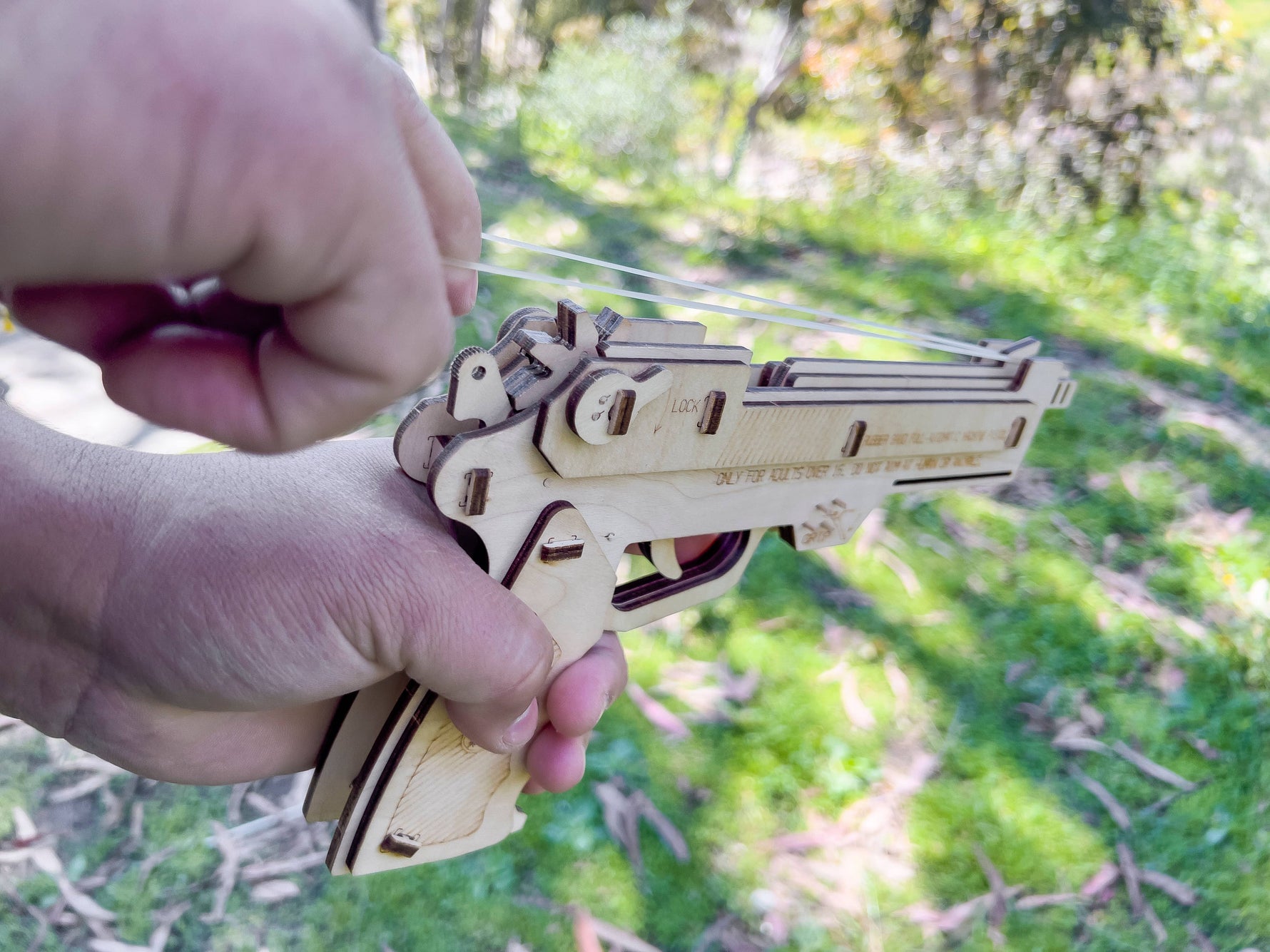 Wooden toy gun held by a hand with a blurred green outdoor background