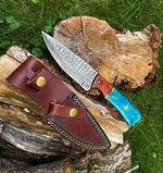 Knife with a blue handle and brown leather sheath on a wooden stump with grass in the background
