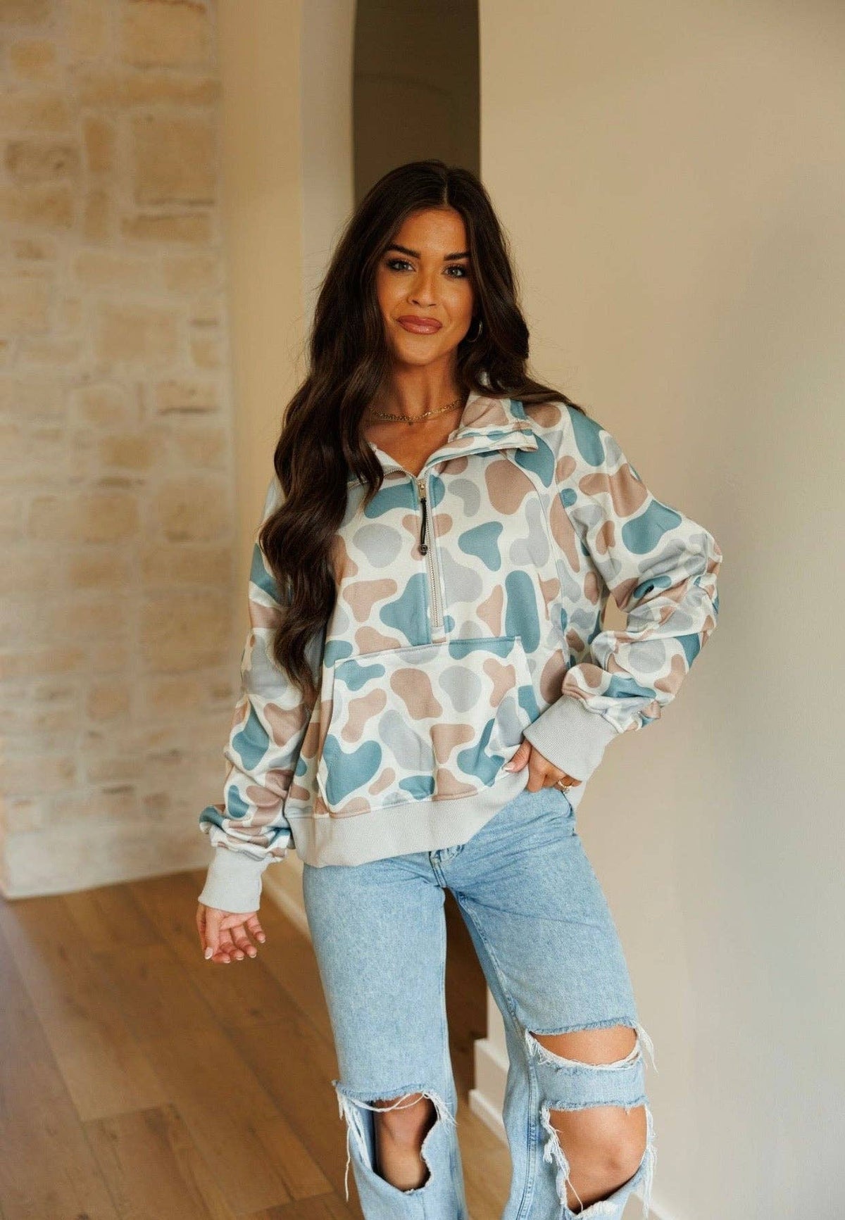 Woman wearing a patterned pullover and ripped jeans indoors.