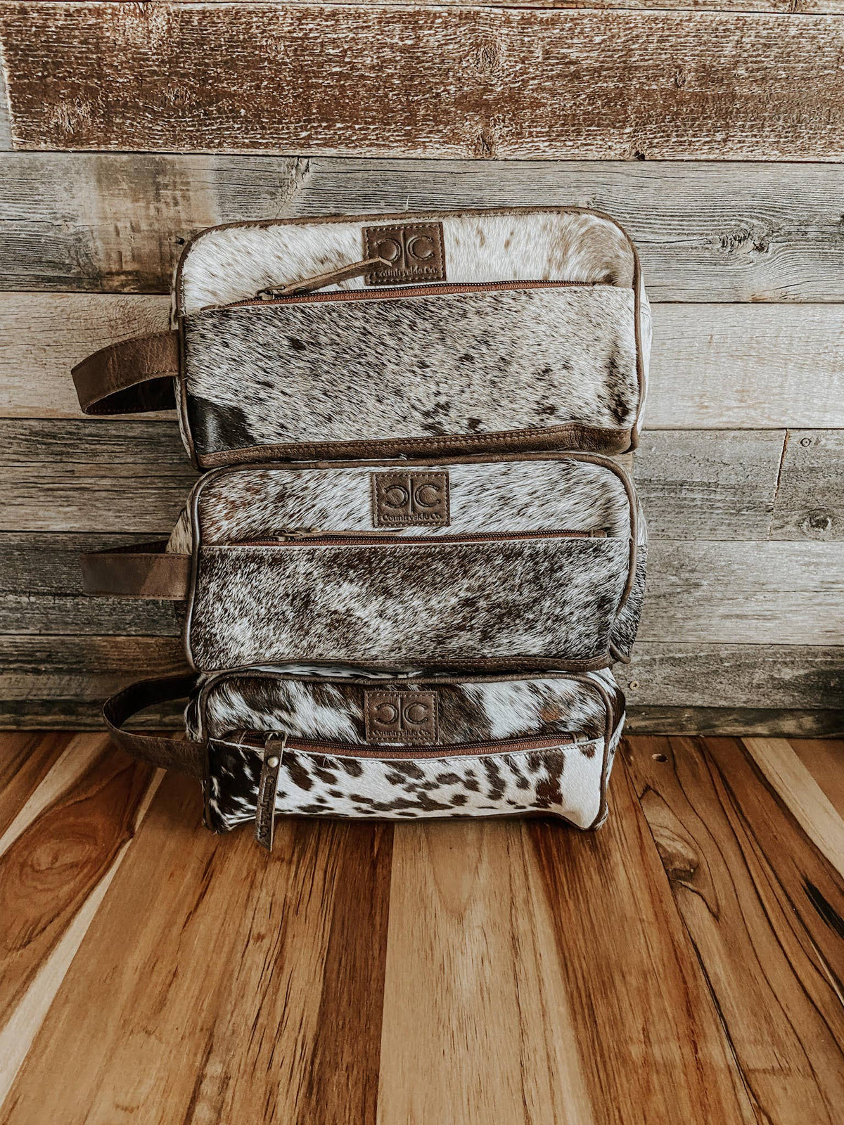 Three cowhide leather bags stacked against a wooden wall.