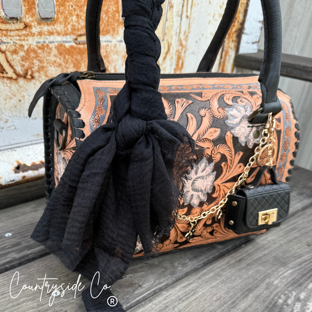 Decorative handbag with intricate patterns and a black scarf draped over it, set against a rustic metal background.