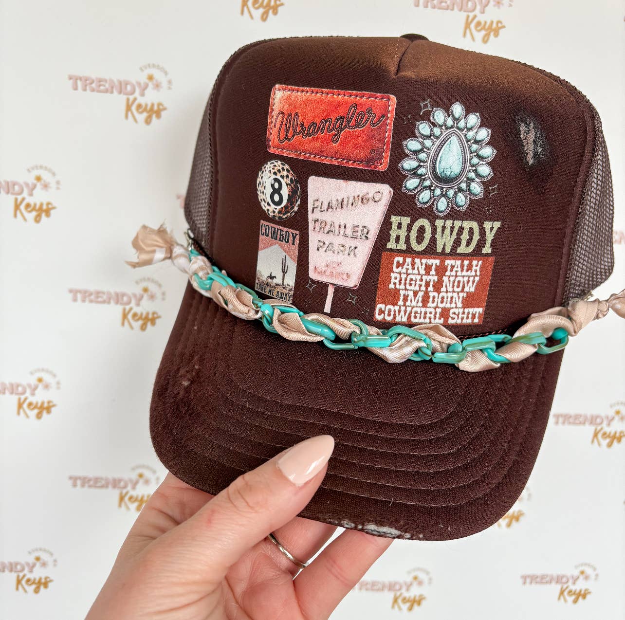 Brown cap with patches and text held by a hand against a branded background
