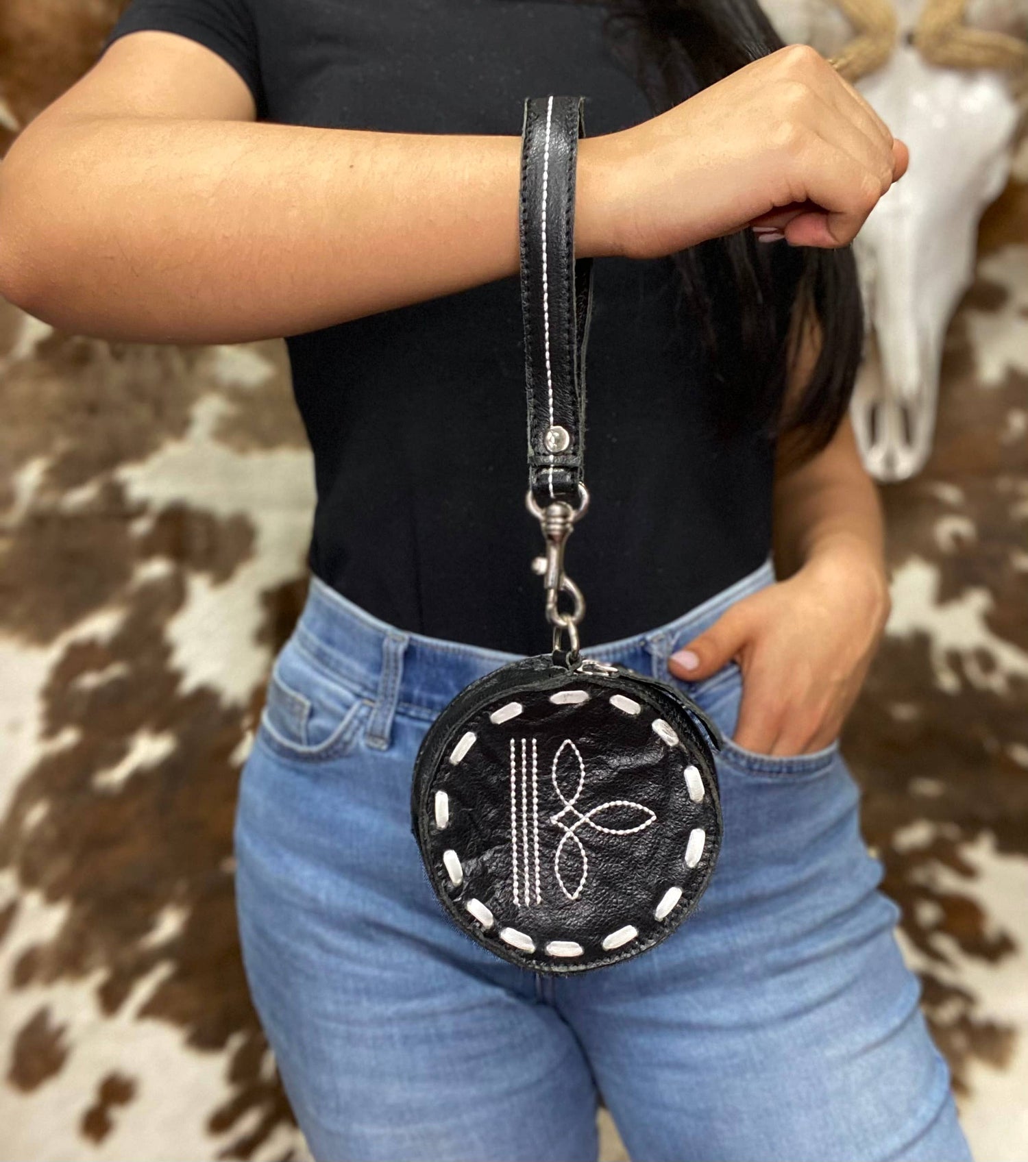 Person holding a black round pouch with white patterns against a cowhide rug background