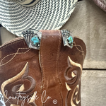 Brown cowboy boot with decorative buckle featuring turquoise stones on a wooden surface, branded 'Countryside Co'.