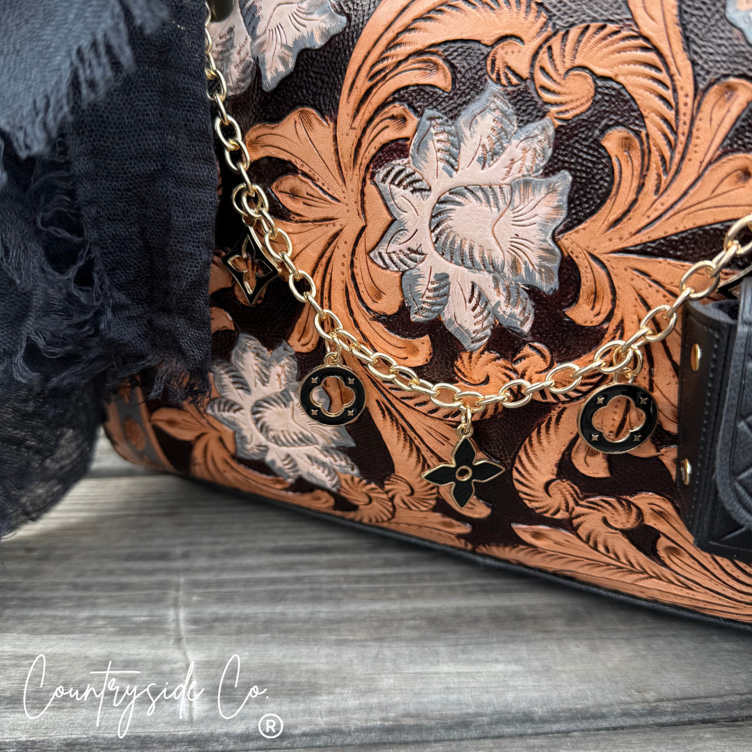 Close-up of a handbag with intricate floral tooled leather design and gold chain strap.