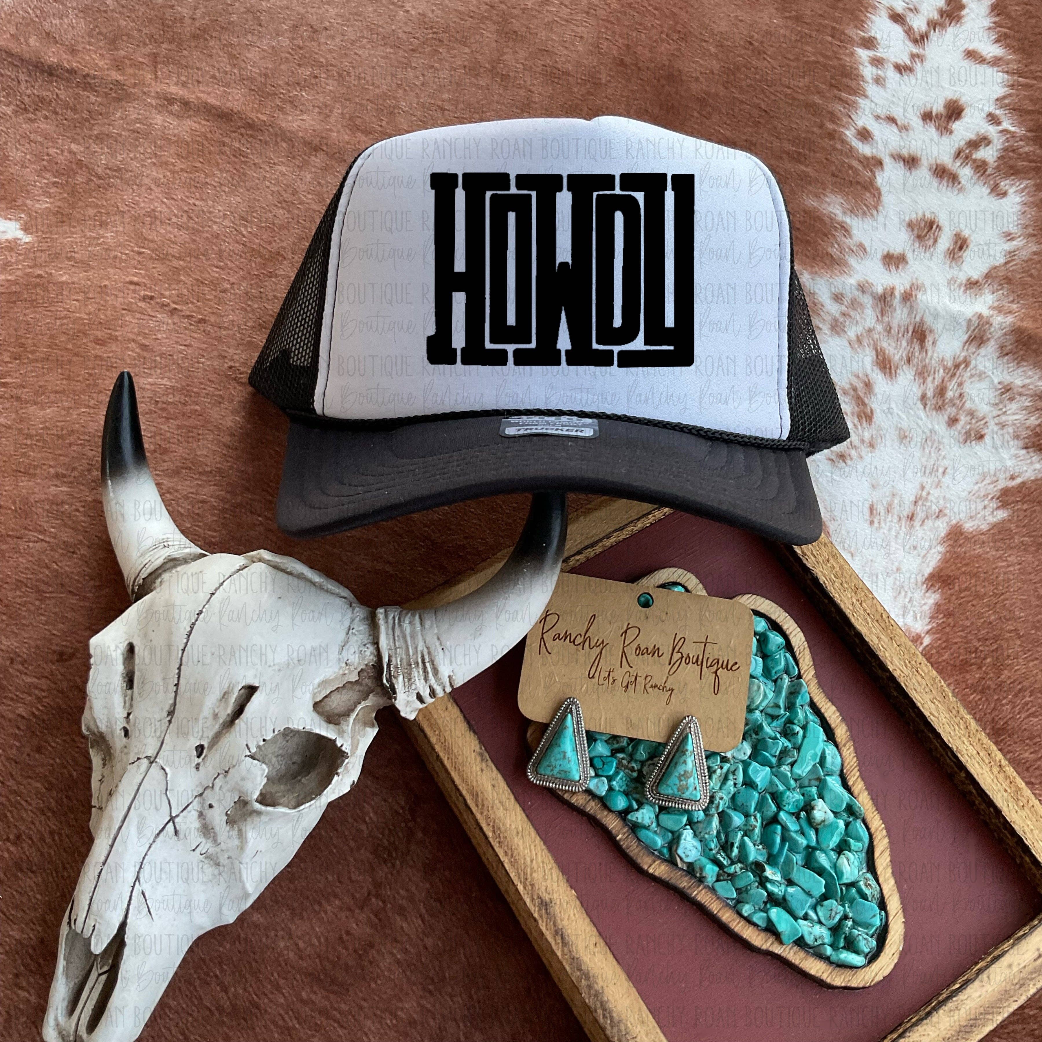Trucker hat with 'HOWDY' text, cow skull, and turquoise earrings on a rustic background