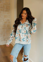 Woman wearing a patterned hoodie and ripped jeans indoors.