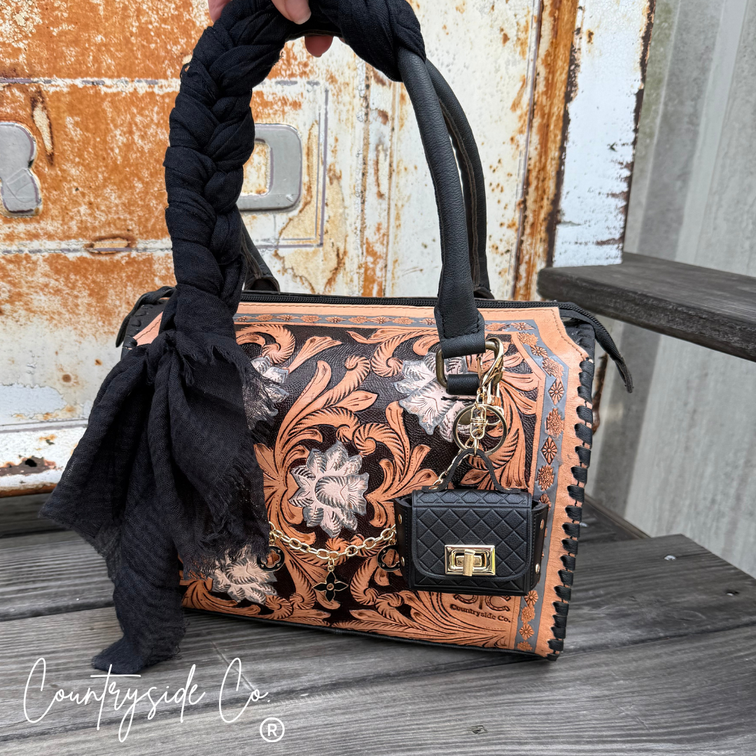 Handbag with intricate designs and a keychain on a wooden surface, featuring the 'Countryside Co' brand.