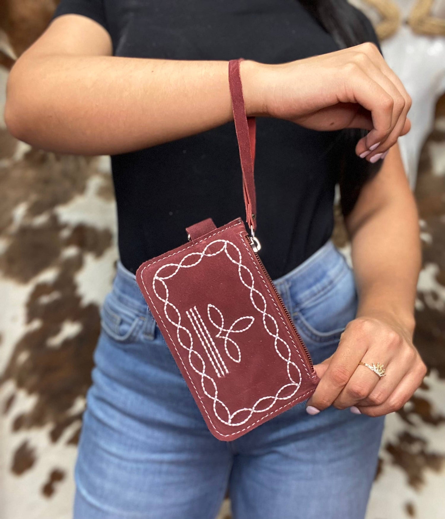 Person holding a maroon embroidered crossbody bag with a cowhide leather background