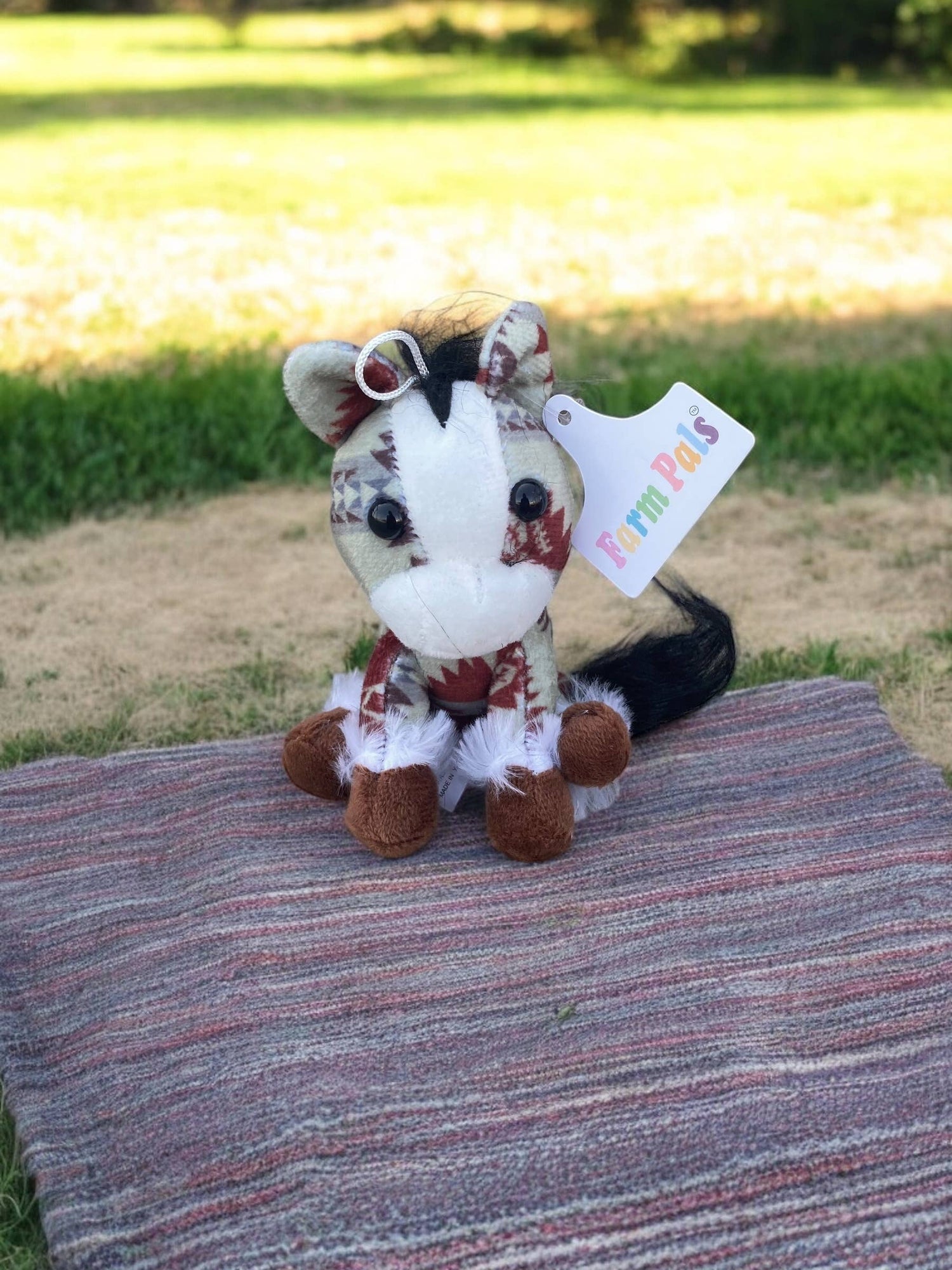 Plush zebra toy with a tag on a striped blanket outdoors