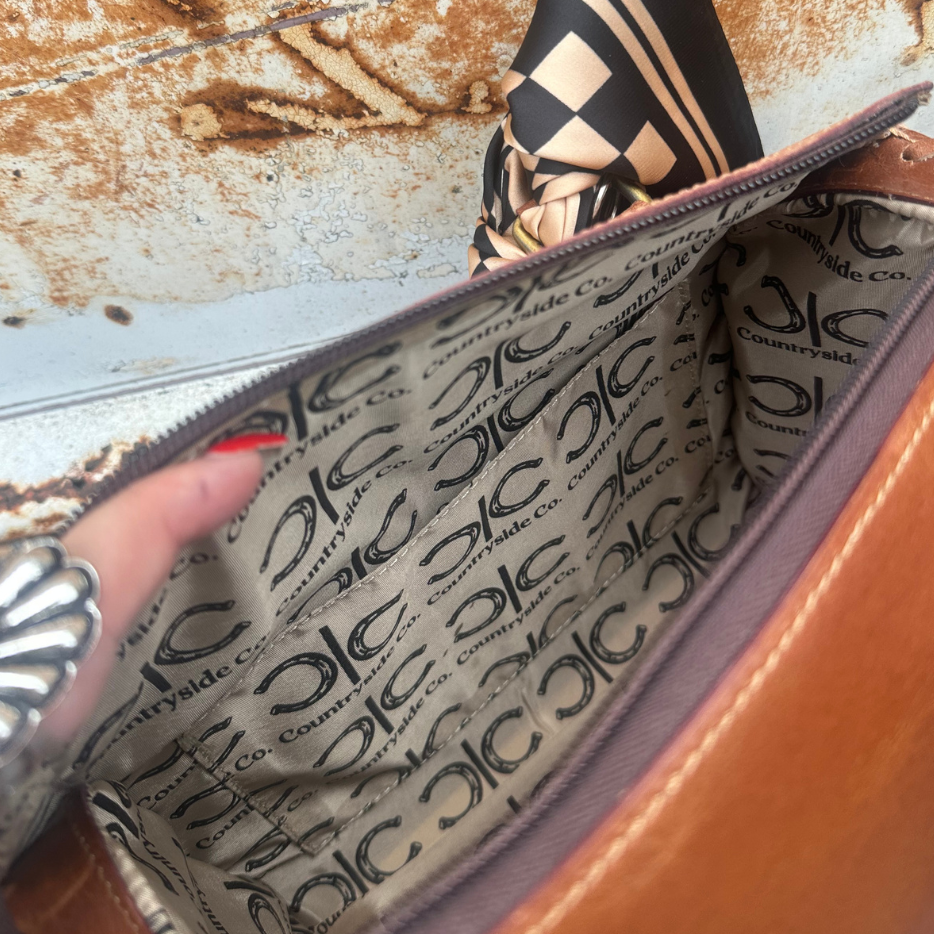 Close-up of a brown leather bag interior with C.C., shown with a hand holding the zipper open.