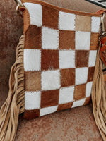 Checkered brown and white handbag with fringes on a textured surface