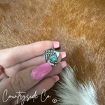 Hand holding a silver ring with turquoise stone against a fur background, featuring 'Countryside Co.' branding.