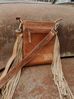 Brown leather handbag with fringes on a textured surface