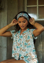 Woman wearing a patterned shirt and headscarf against a wooden background