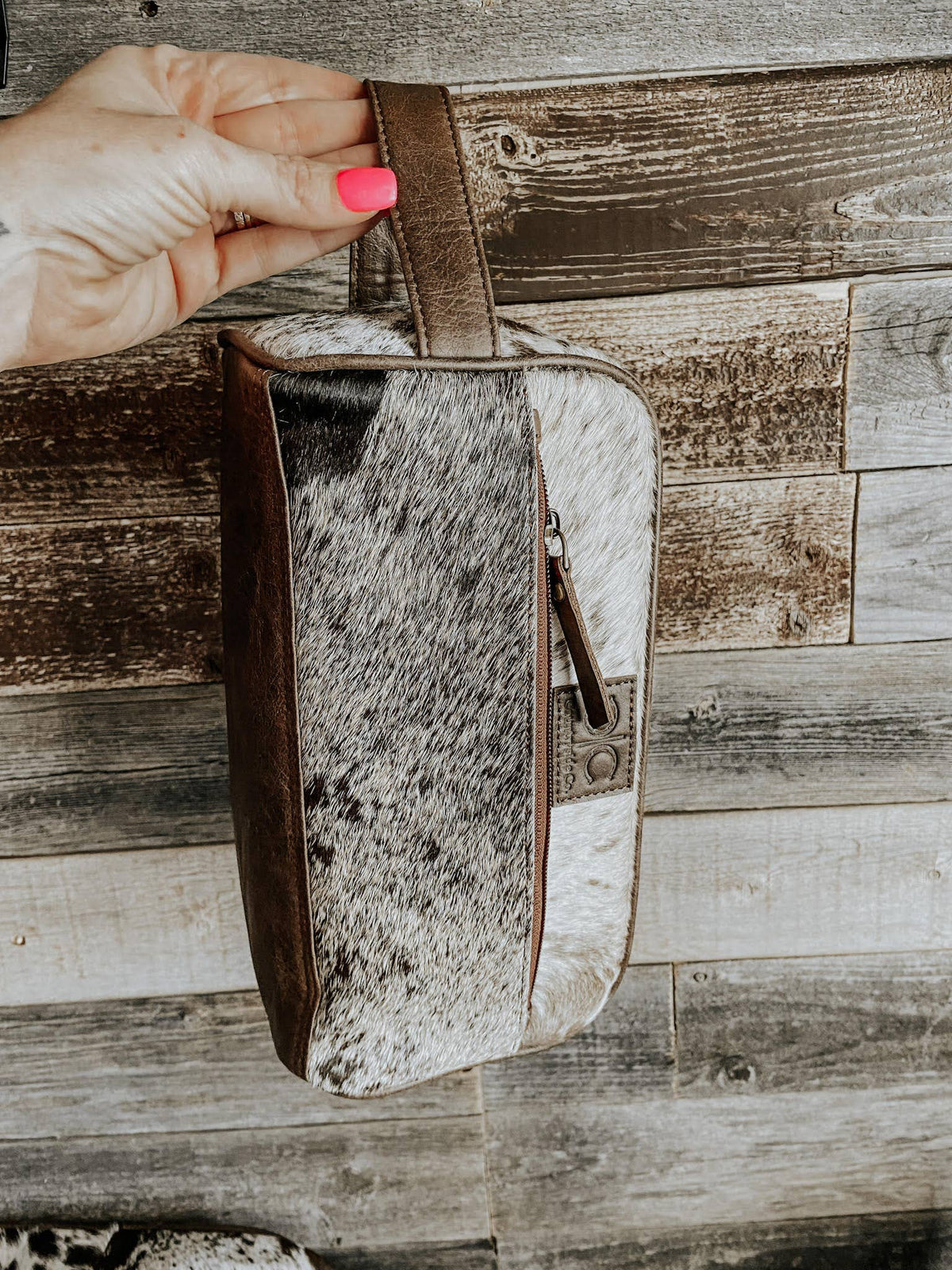 Hand holding a cowhide leather pouch against a wooden background