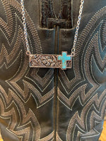 Necklace with a turquoise cross pendant on a leather surface with intricate patterns