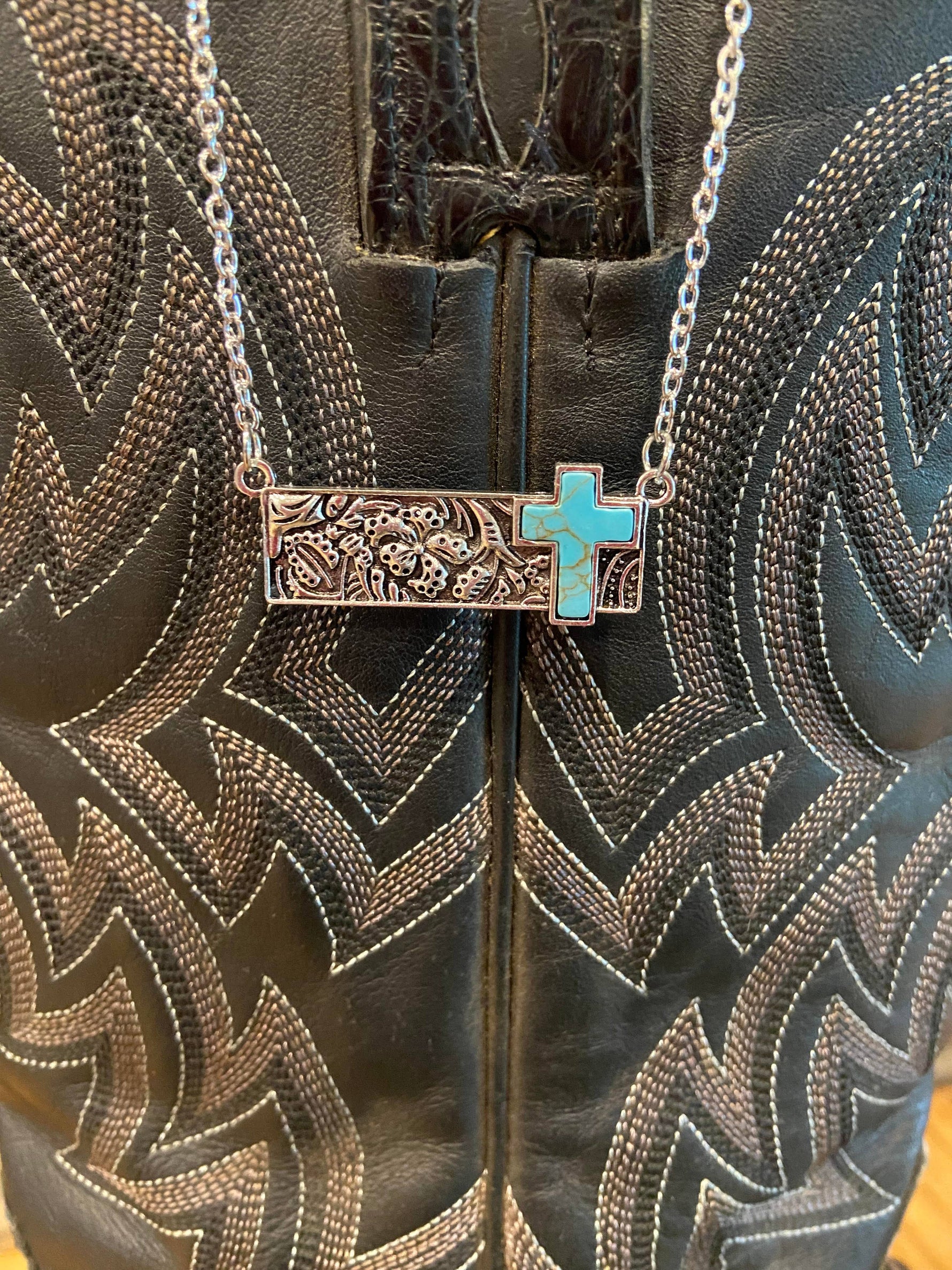 Necklace with a turquoise cross pendant on a leather surface with intricate patterns