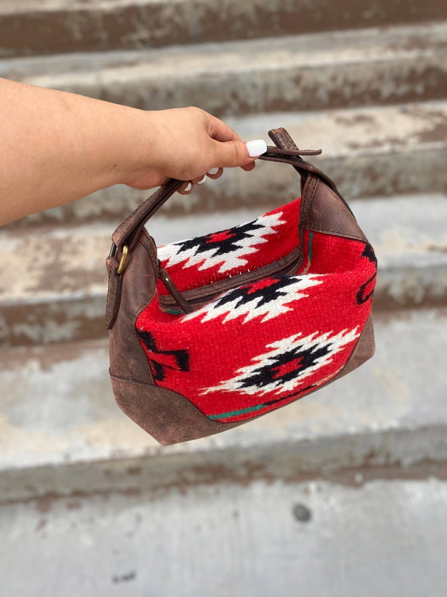 Handbag with red and brown pattern held by a hand on a metal surface