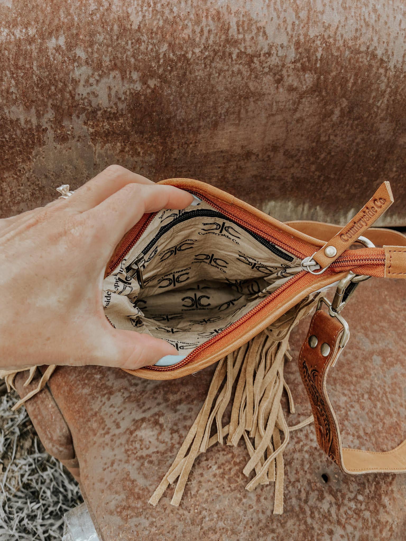 Hand holding a brown leather bag with fringe against a rustic background