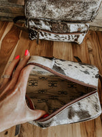 Cowhide leather handbag with a hand opening it on a wooden surface
