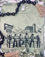 Green t-shirt with a graphic of cowboys and a barn, surrounded by decorative elements.