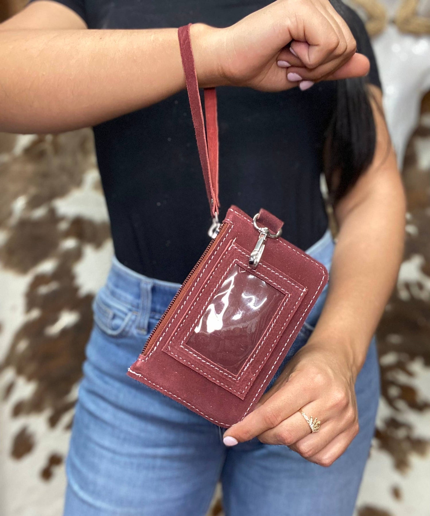 Person holding a maroon wallet with a clear window against a cow print background