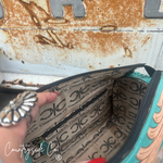 An open turquoise and beige patterned zippered pouch or cosmetic bag, shown with a hand inside. The interior lining has a repeating black 'Countryside Co' logo pattern.
