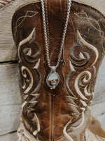 Close-up of a brown embroidered boot with a necklace hanging from it, on a wooden surface.