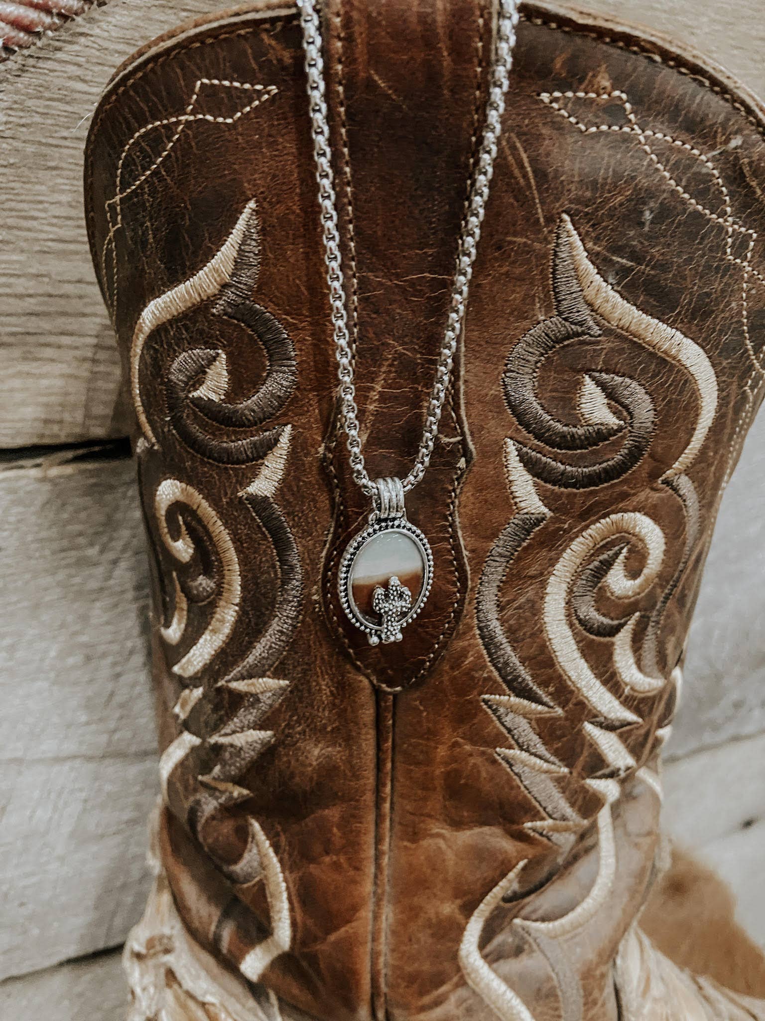 Close-up of a brown embroidered boot with a necklace hanging from it, on a wooden surface.